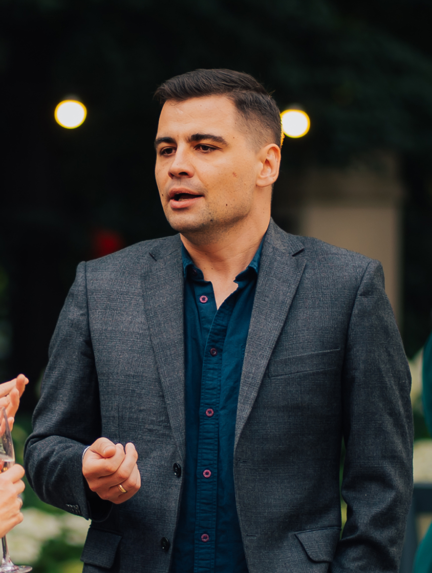 A man dressed in a gray suit, exuding professionalism and elegance, stands confidently with a neutral background.